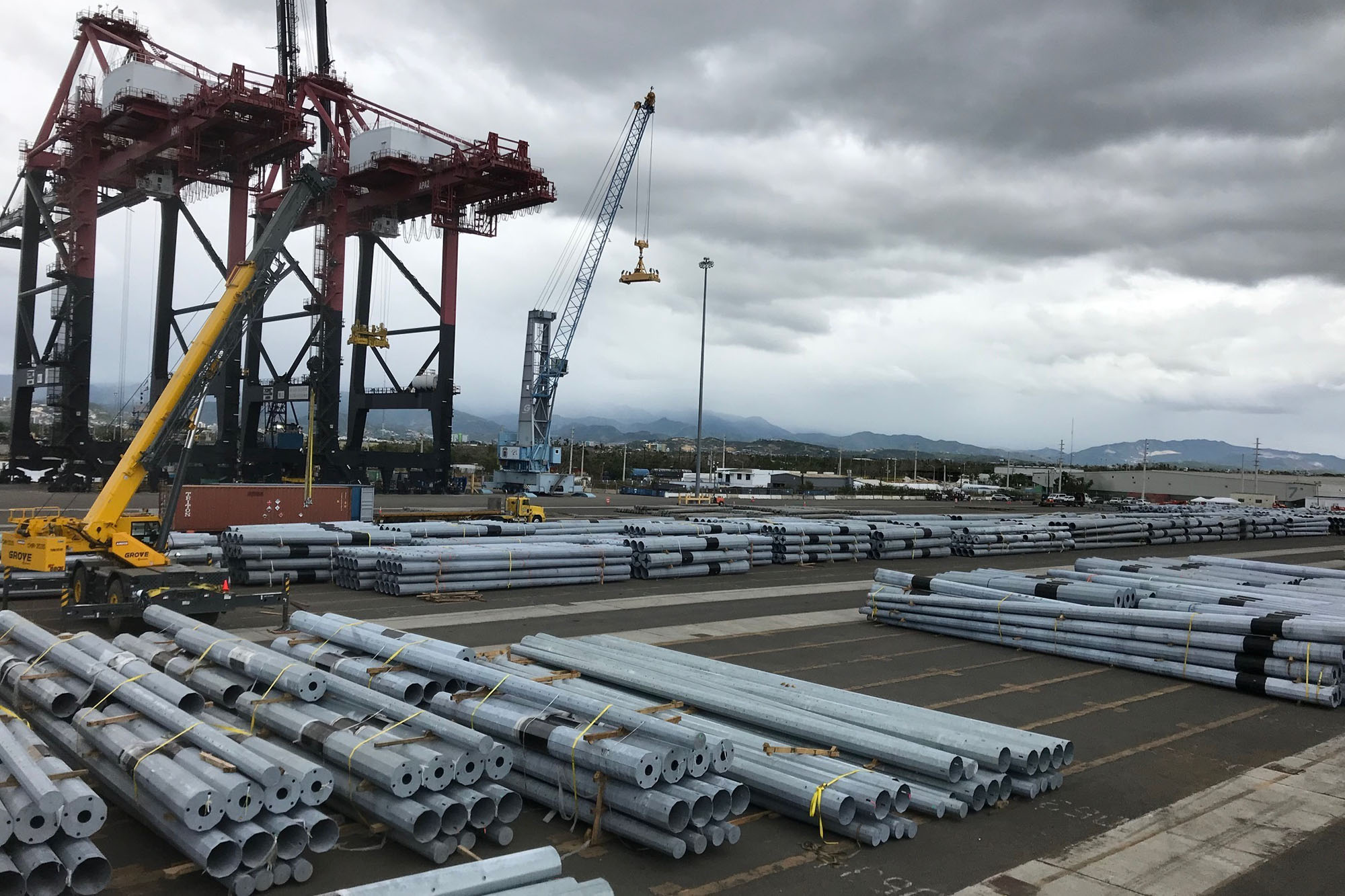 Large piles of power poles on a dock with large unloading equipment